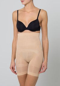 Beige high-waisted shaping shorts made from stretchy, lightweight fabric. Features a seamless design and ribbed waistband for support.