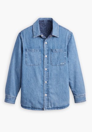 Camisa de ganga de cor azul clara, com fecho frontal por botões, dois bolsos no peito e um forro interior padrão em azul escuro. Apresenta gola.