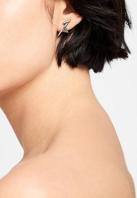 Boucles d'oreilles en métal en forme d'éclair noir. Présentent une finition polie et un design géométrique. Portées dans l'oreille.