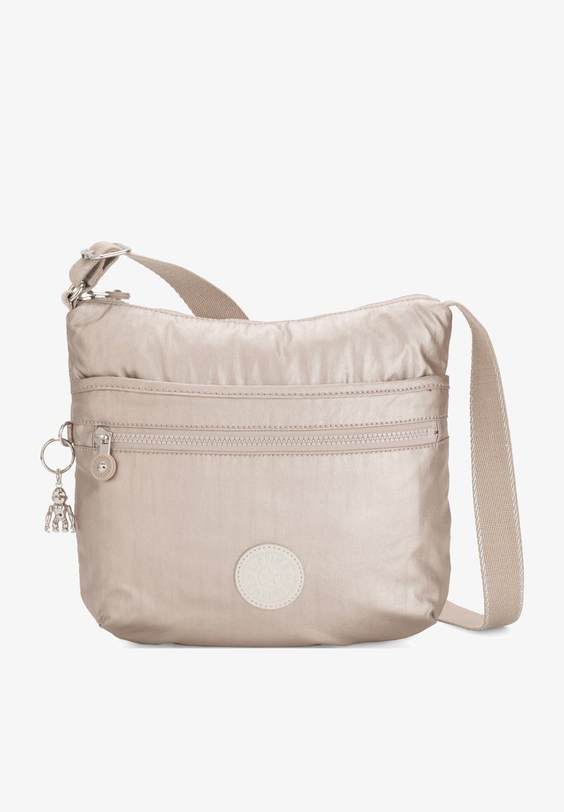 Beige schoudertas gemaakt van soepel materiaal; heeft een ritsvak aan de voorkant, een verstelbare schouderriem en een ronde logo-accent.
