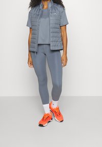 Gray athletic outfit featuring a short-sleeve top, fitted leggings, and a puffy vest. Bright orange athletic shoes with white accents.