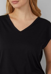 Vrouw in een zwart mouwloos topje met V-hals, die hals, schouders en bovenborst laat zien, met lichte huid en sproeten.