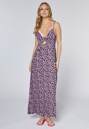 Woman wearing a pink leopard print maxi dress with thin straps and a front cutout, standing barefoot against a plain background.