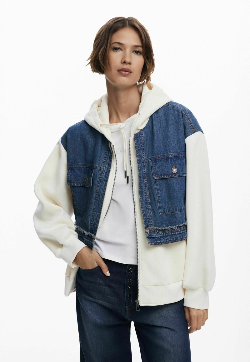 Giacca di jeans con felpa bianca con cappuccio. Presenta tasche frontali, chiusura con zip e colori a contrasto. Tessuto liscio e design casual.