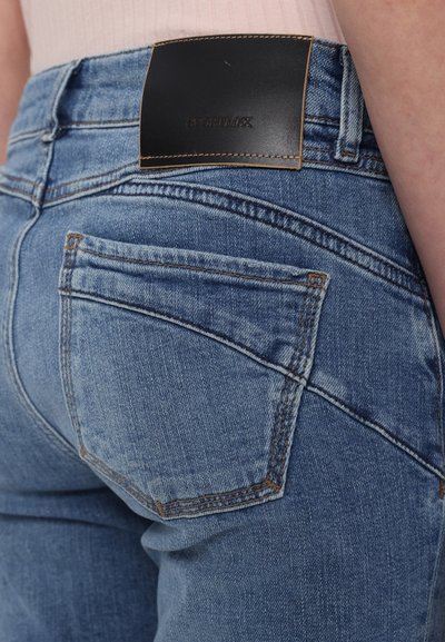 Os jeans de ganga azul claro apresentam uma cintura alta, costura distinta nos bolsos e um remendo de pele preta na parte de trás da cintura.