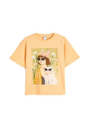 Gul bomulds T-shirt med et farverigt illustreret print af en kvinde og en kat, der bærer solbriller, omgivet af blomsterlige elementer.