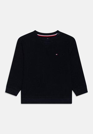 Maglietta a maniche lunghe ribbed blu scuro con scollatura rotonda e interno a contrasto, caratterizzata da un piccolo logo sul petto. Dettaglio con bottoni sulla spalla.