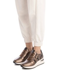Zapatillas de color bronce con acabado metálico, acentos negros en contraste y cordones marrones; suela de cuña blanca y detalle de cremallera en el lateral.
