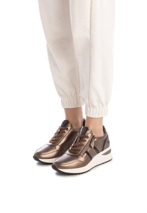 Zapatillas de color bronce con acabado metálico, acentos negros en contraste y cordones marrones; suela de cuña blanca y detalle de cremallera en el lateral.