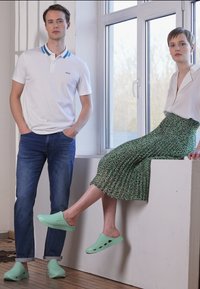 Camisa pólo branca com detalhes azuis, jeans azuis e sapatos slip-on verde menta. Modelo em uma blusa branca e saia plissada verde com padrão.