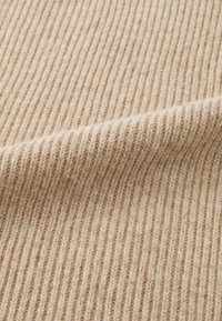 Tissu en tricot côtelé beige avec une texture douce et des variations subtiles de couleur, présentant des lignes verticales fines et régulièrement espacées tout au long.