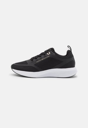Sort atletisk mesh-sneaker med hvid sål, snøredesign, trække-flap ved hælen, og "Tommy Hilfiger"-logo på siden.