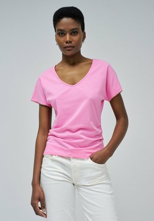 Camiseta rosa de algodón suave con cuello en V, mangas cortas y detalle sutil en el borde, combinada con pantalones blancos. Textura suave y ajuste casual.