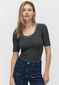 Mørkegrå kortærmet bodystocking med en scoop halsudskæring, der har blomster-lace kant; sat sammen med højhalsede blå denimjeans.