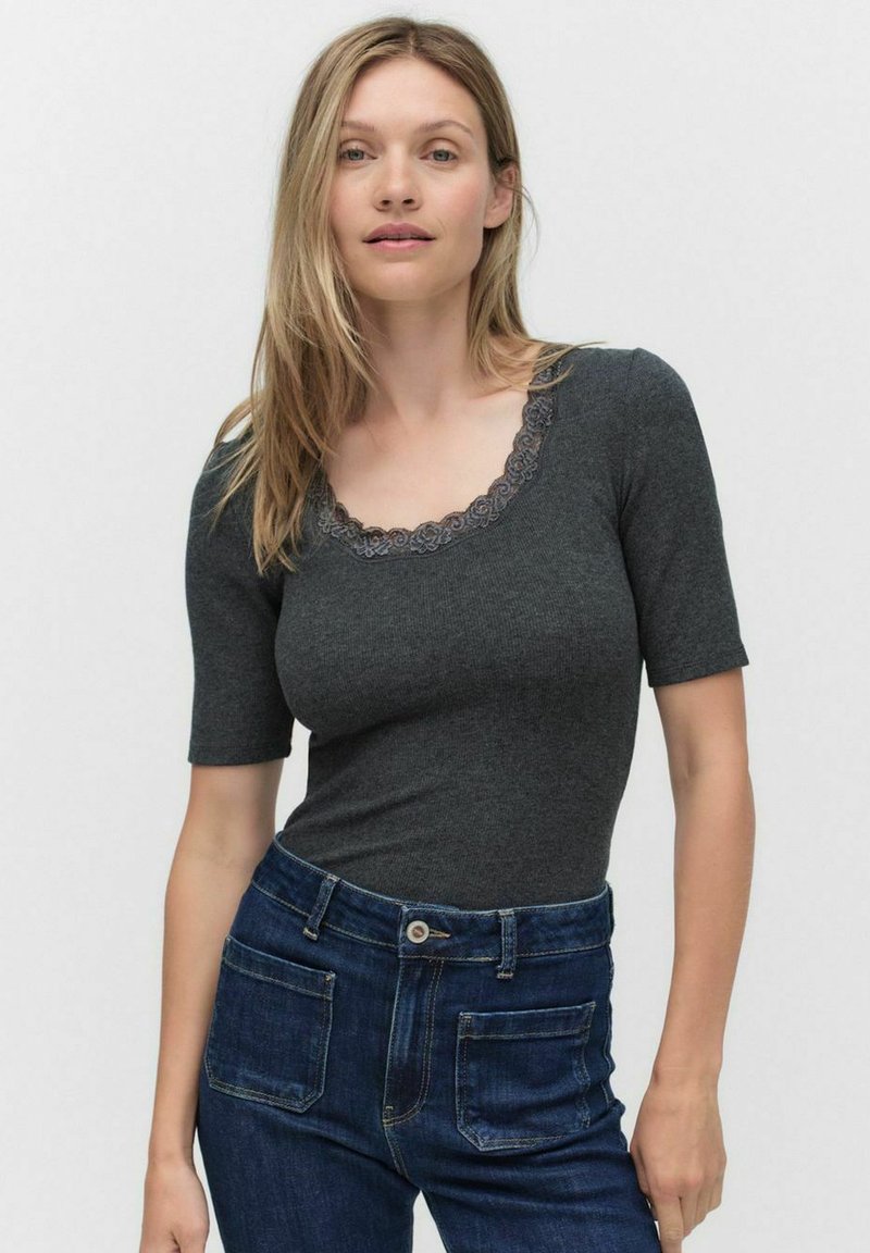 Mørkegrå kortærmet bodystocking med en scoop halsudskæring, der har blomster-lace kant; sat sammen med højhalsede blå denimjeans.