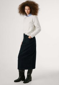 Hellgrauer Strickpullover, dunkelblaue Jeansrock in Hochbundform und knielange schwarze Lederstiefel. Einfaches Design, glatte Textur und subtile Details.