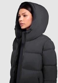 Black puffer jacket with a large hood, zip closure, and external branding. The material appears smooth and padded, designed for warmth.