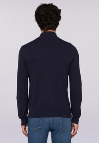 Námořnická modrá svetr s dlouhými rukávy a límečkovým designem, který se vyznačuje hladkou texturou a žebrovanými manžetami a lemem. Zadní pohled ukazuje přiléhavý siluetu.