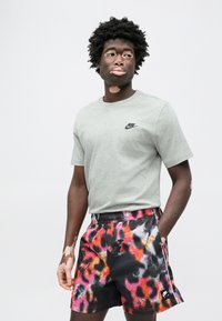 Γκρι βαμβακερό μπλουζάκι με μαύρο λογότυπο Nike, συνδυασμένο με μαύρο σορτς με πολύχρωμο αφηρημένο μοτίβο σε κόκκινο, πορτοκαλί και ροζ.