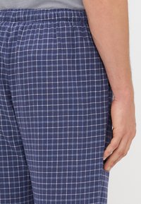 Pantalones de pijama em xadrez azul marinho em tecido leve com cintura elástica, apresentando um padrão em grelha em azul e branco.