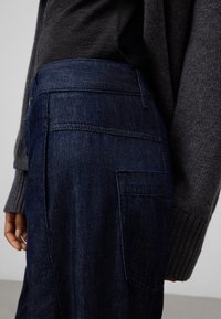 Mörkblå denimbyxor med rak passform, med en lapplåda och subtila sömnadsdetaljer. Bärs med en grå stickad tröja.