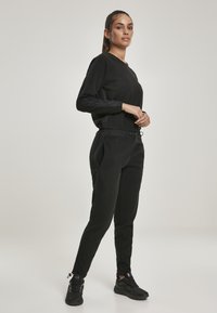 Conjunto de dos piezas negro que incluye una blusa de manga larga y pantalones ajustados, confeccionado en una tela suave. Detalles incluyen cintura elástica y bolsillos laterales.