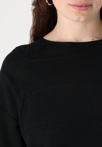 Black sweater with a textured finish, featuring a round neckline and subtle seam details on the shoulders and chest area.