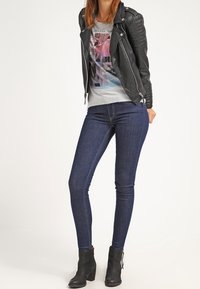 Black leather biker jacket with quilted shoulder accents, gray graphic T-shirt, dark blue skinny jeans, and black ankle boots.