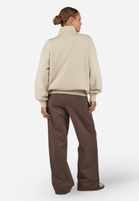 Pulover bej cu guler înalt și siluetă supradimensionată, asortat cu pantaloni brun deschis largi. Design minimalist, textură moale și culori neutre.