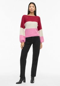 Maglione lavorato a maglia con strisce orizzontali bordeaux, bianche, rosa e rosa chiaro; maniche a palloncino larghe e una vestibilità comoda. Abbinato a jeans neri.
