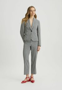 Černobílý kostkovaný blazer s odpovídajícími zkrácenými kalhotami, se zapínáním na jedno tlačítko a přiléhavým střihem. Doplněno červenými balerínami.