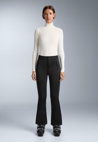 Crne široke hlače s prednjim zip džepovima, glatke teksture i uskim pojasom. Uparene s uskim bijelim dugim rukavima rolak majicom.