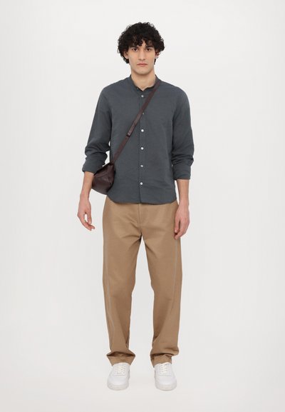 Dunkelgraues Langarmshirt, khakifarbene Hose, weiße Sneaker und eine braune Umhängetasche. Glatter Stoff, gerade Passform, einfaches Knopfdesign.