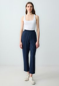 Hosen aus leichtem, navyblauem Stoff mit einem elastischen Bund, taillierte Beinform, kombiniert mit einem weißen Tanktop und weißen Sneakers.