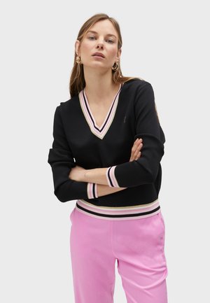 Sweater noir avec un col en V, orné de rayures roses, crème et noires au niveau de l'encolure et des manches. Associé à un pantalon rose.