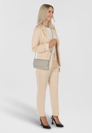 Completo sartoriale beige con blazer strutturato e pantaloni aderenti. Completato da una borsa a tracolla grigio chiaro e décolleté nere. Tessuto dalla texture liscia.