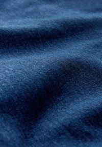 Denimstoff in einem tiefen Marineblau, mit einer weichen Textur und subtilen Variationen und Falten, die das gewebte Muster hervorheben.