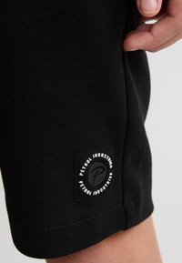 Pantalones cortos de algodón negros con una etiqueta de logo visible que dice "Petrol Industries". La tela tiene una textura suave y el dobladillo está acabado de manera prolija.