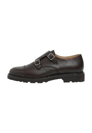 Chaussure monk strap en cuir brun foncé avec deux boucles argentées et une semelle épaisse en caoutchouc noir, vue de côté sur un fond blanc.
