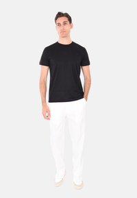 T-shirt nera a maniche corte abbinata a pantaloni bianchi, che mette in mostra un design semplice. Il modello è in piedi su uno sfondo neutro. Sneakers bianche completano il look.