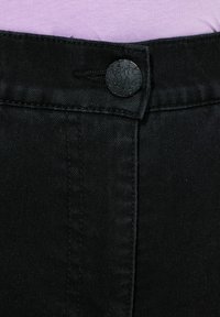 Pantalones de mezclilla negros con cierre de botón y detalles de costura sutiles. Tejido texturizado, mostrando un primer plano de la cinturilla y el botón.