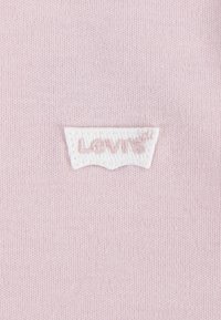 Svijetlo ružičasta tkanina s glatkom teksturom, koja prikazuje bijelu Levi's oznaku u obliku luka na donjem centru.