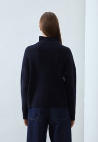 Marineblauer, gestrickter Rollkragenpullover mit lockerem Schnitt und gerippter Struktur. Verfügt über überschnittene Schultern und einen geraden Saum. Wird mit dunkler Jeans getragen.