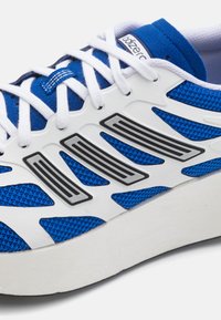 Blå mesh löparskor med vita och svarta accenter, med en texturerad ovandel, tjock vit sula och kontrasterande horisontella ränder.