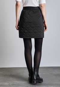 Schwarzer gesteppter Rock mit strukturiertem Finish, elastischem Bund und A-Linien-Silhouette, kombiniert mit schwarzen Strumpfhosen und Stiefeletten.