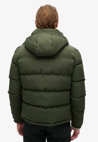 Giacca piumino verde con cappuccio, caratterizzata da un design a trapunta, polsini elasticizzati e un logo sulla parte alta della schiena. Tessuto liscio, materiale isolante.