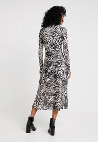 Långärmad klänning med zebramönster i svart och beige, midi-längd med en figurnära silhuett. Bärs med svarta ankelboots med kraftiga klackar.