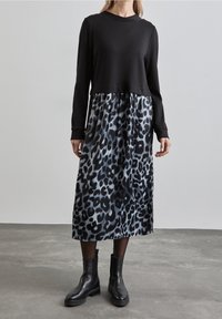 Svart långärmad topp ovanför en leopardmönstrad kjol i nyanser av grått och svart, matchad med svarta ankelskor. Slät tygkvalitet.