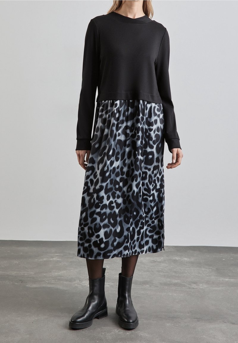 Svart långärmad topp ovanför en leopardmönstrad kjol i nyanser av grått och svart, matchad med svarta ankelskor. Slät tygkvalitet.