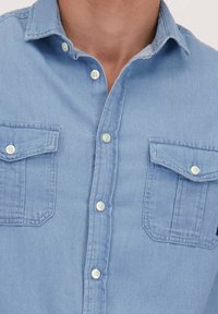 Lichtblauw chambray overhemd met een button-down kraag, twee borstzakken met klep en witte knopen met een soepele textuur.
